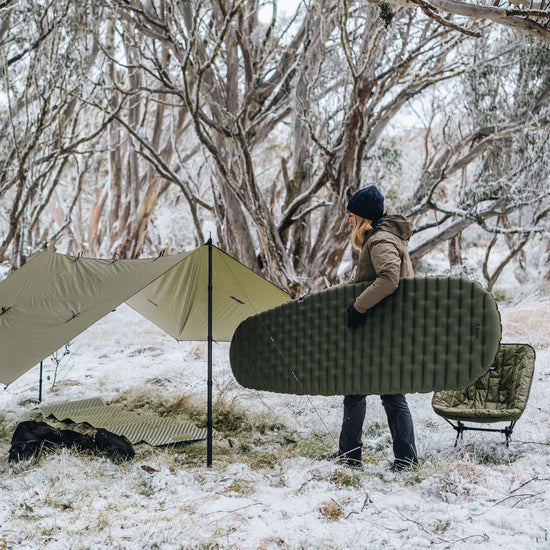Woman places sleeping mat into camping tarp shelter in snow