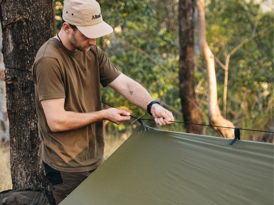 Man securing camping tarp ridgeline