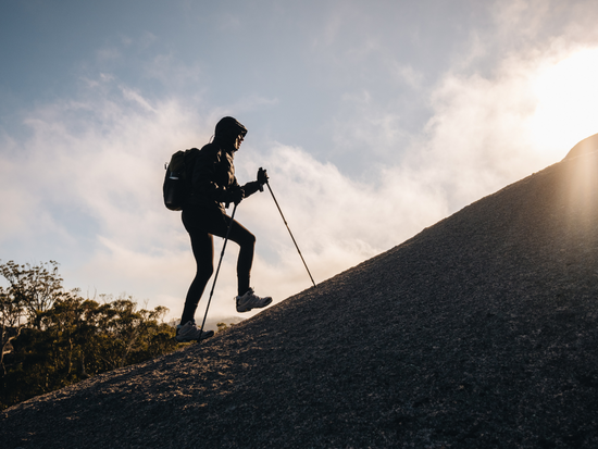 Woman hikes uphill with hiking poles.