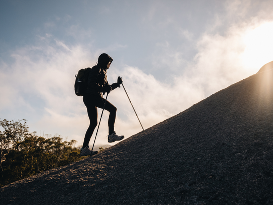 Woman hikes uphill with hiking poles. 